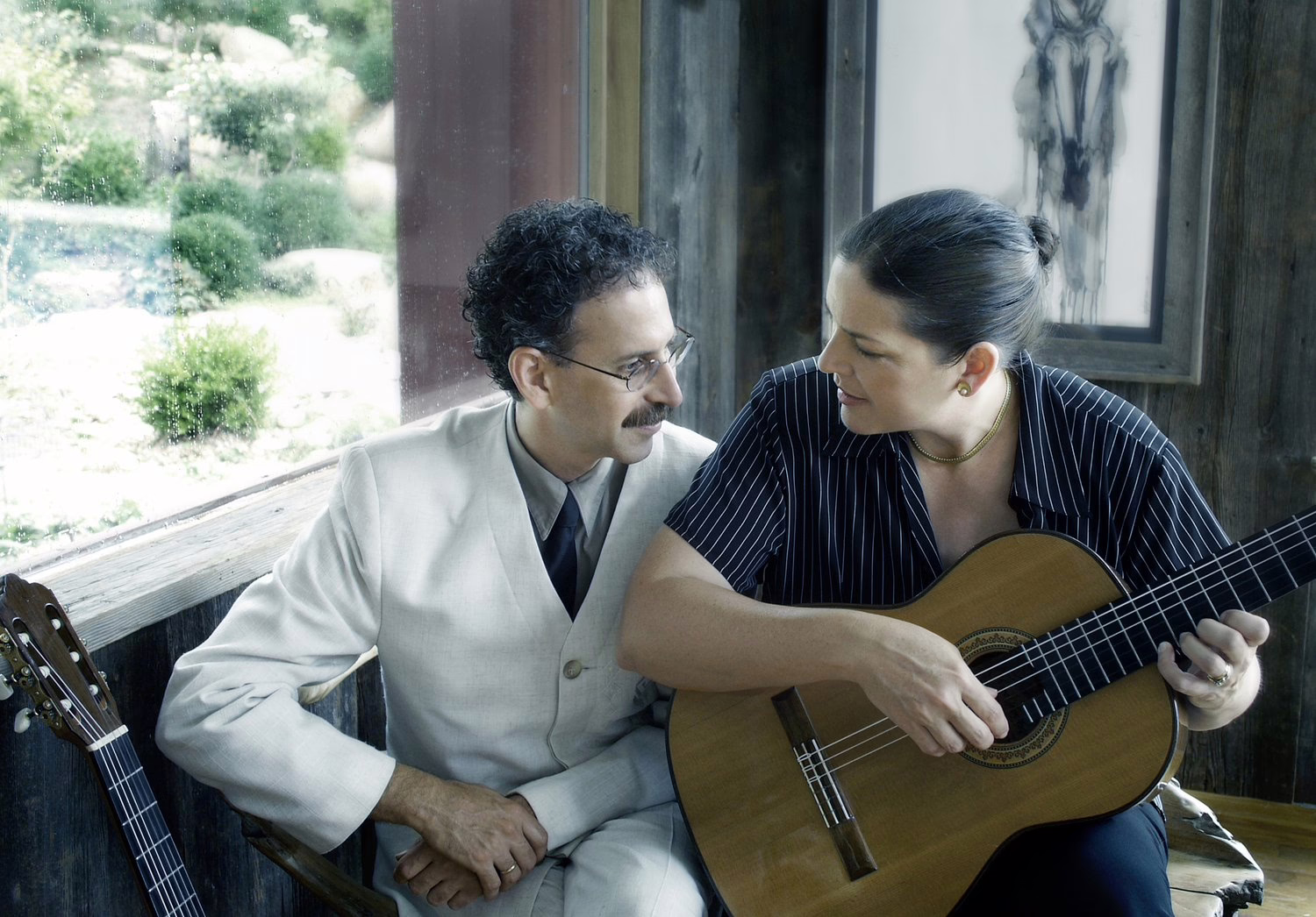 A man and a woman look at each other while the woman plays acoustic guitar.
